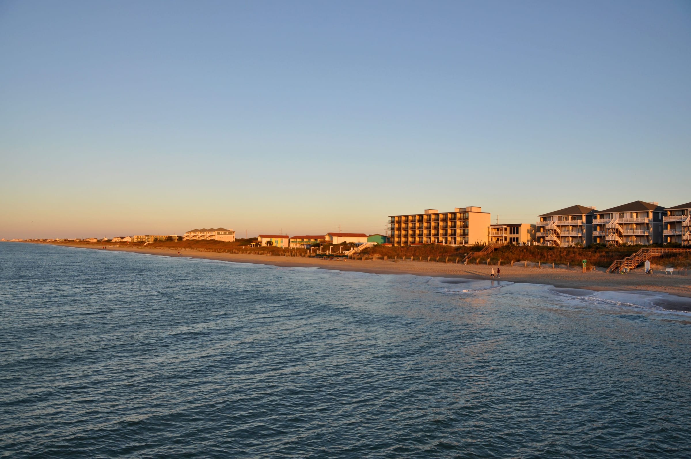 The shoreline at Atlantic Beach in evening light, hotels and houses along the beach, calm water in the foreground