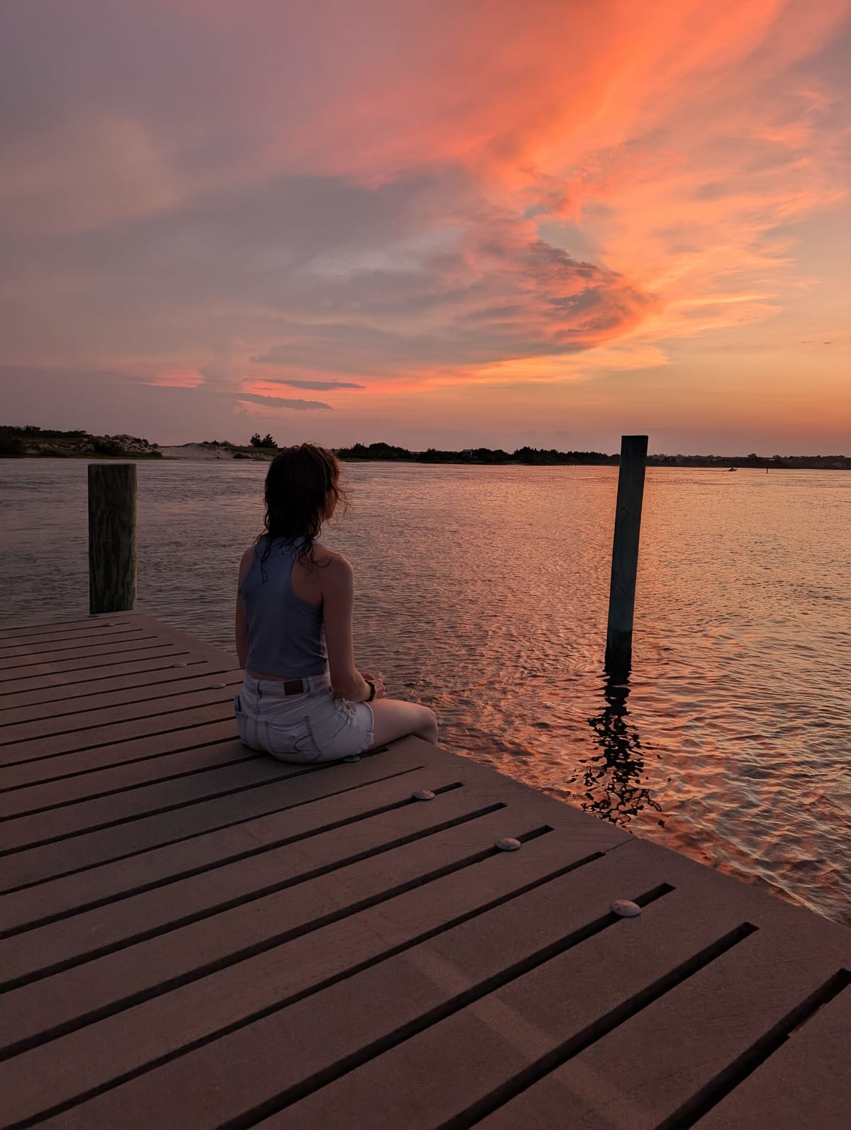 A person sitting at the end of a wooden dock at Cedar Point, looking out over still water under an orange and pink sunset