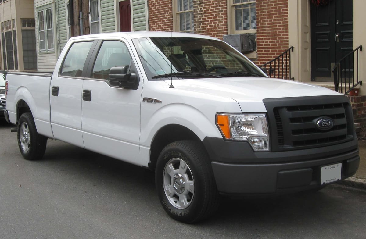 A white crew-cab pickup truck parked on a town street in front of brick row houses