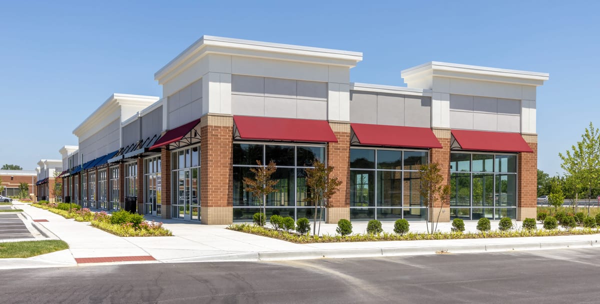 A newly built strip plaza with brick and stone storefronts, red awnings and an empty parking lot, before its first tenants