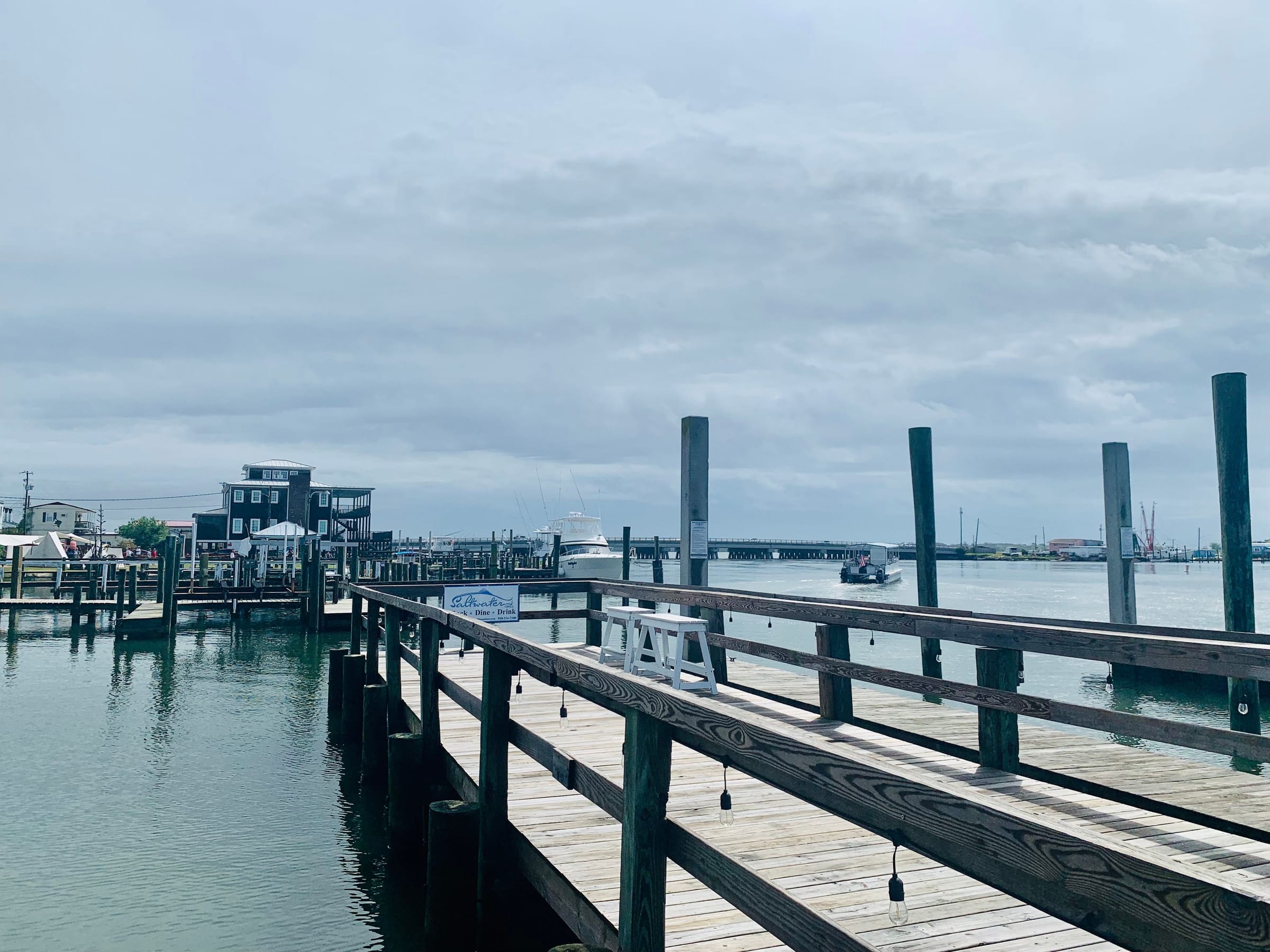 A wooden dock with tall pilings on the Swansboro waterfront, boats moored beyond under an overcast sky