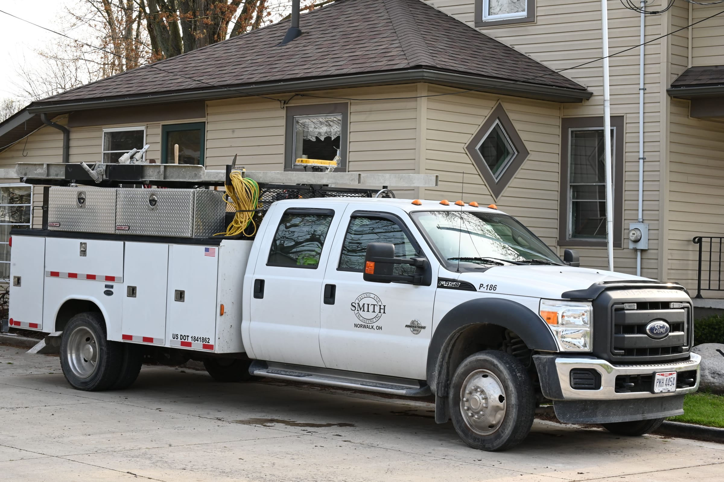 A white crew-cab work truck with a service body of tool compartments parked beside a house